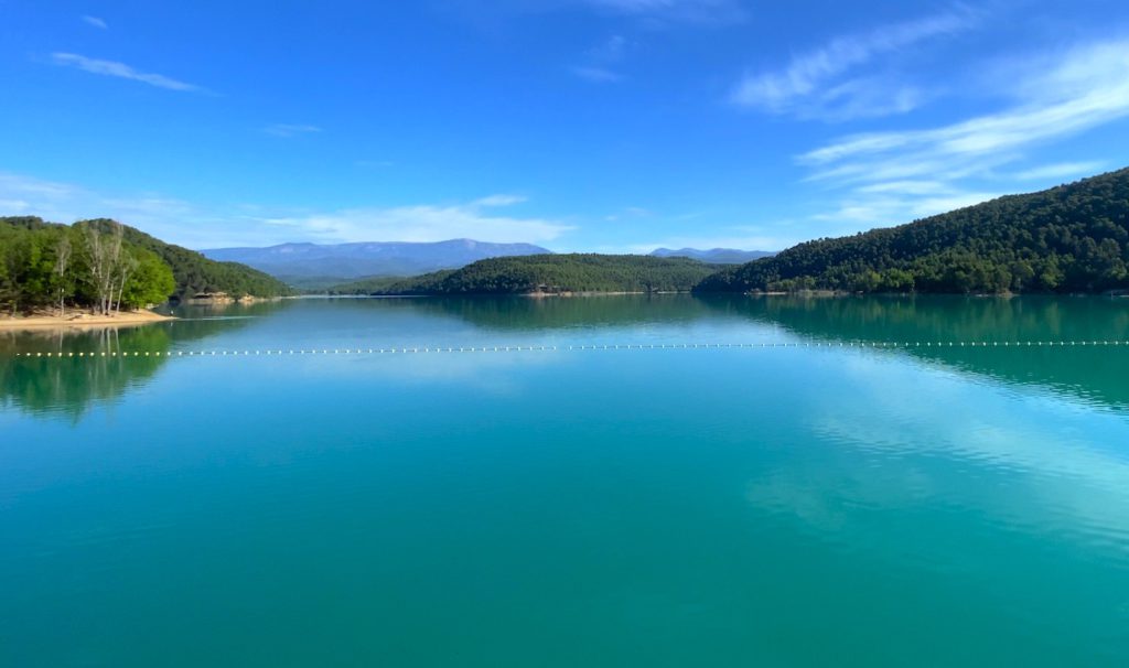 Paisaje de un lago, con vegetación a los lados y montañas al fondo