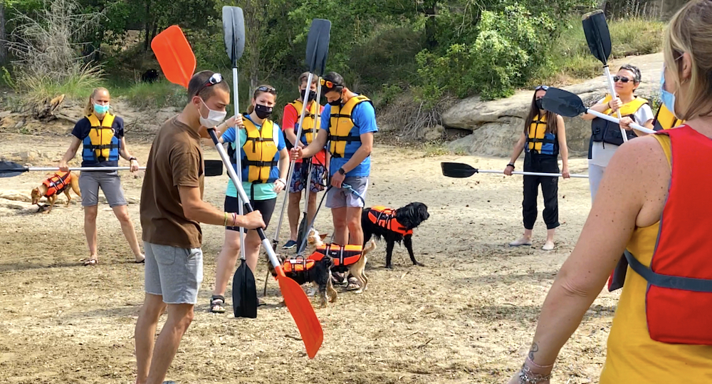 Persona enseñando a usar un remo de kayak a un grupo de personas, todas con chaleco salvavidas